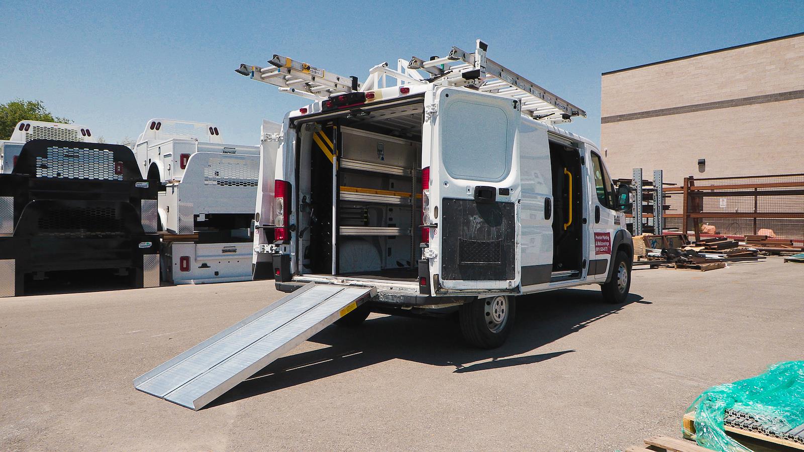 2025 ProMaster (VF) 2500 Tradesman 159-inch Wheelbase Premier Painting Cargo Van with High Roof in Bright White with open doors showing Ranger Shelving & Ladder Racks with ramp, parked on asphalt outside of a building, clear sky visible beyond.